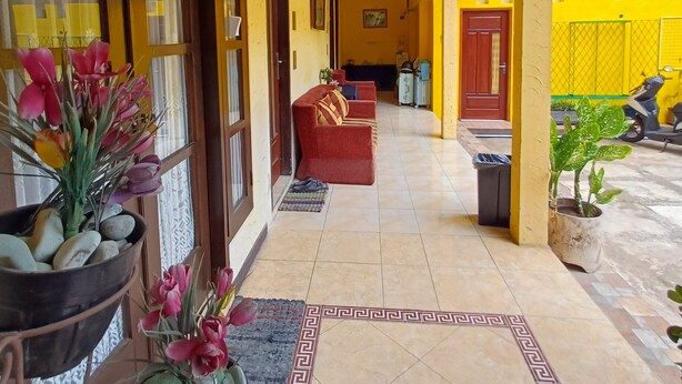 A corridor with a tiled floor, a red sofa, potted plants, and air conditioning units. - Irma Guest House (Malang)