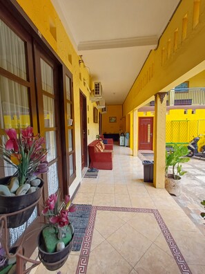 A corridor with a tiled floor, a red sofa, potted plants, and air conditioning units. - Irma Guest House (Malang)