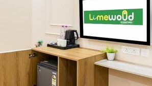 A hotel room with a wooden desk, a small refrigerator, a coffee maker, and a television displaying the Limewood Signature logo.
