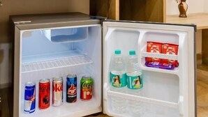 A compact refrigerator with beverages and snacks inside, a coffee maker, and a small potted plant on the counter.