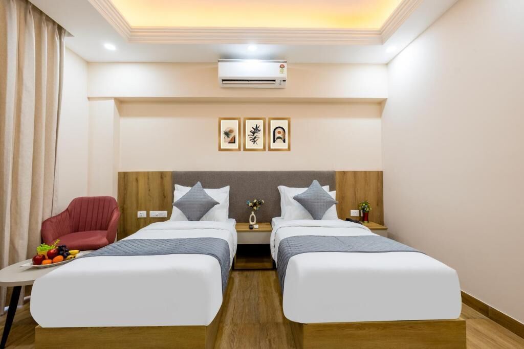 A hotel room with two beds, a red chair, a small table with fruit, and wall art.