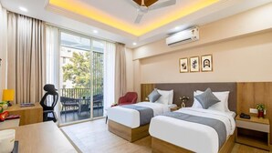 A hotel room with two beds, a desk, a chair, an air conditioning unit, and a balcony with a view of the outside.
