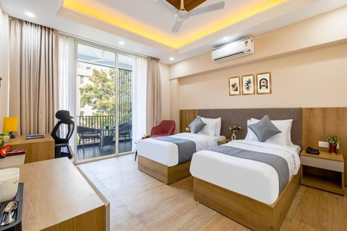 A hotel room with two beds, a desk, a chair, an air conditioning unit, and a balcony with a view of the outside.