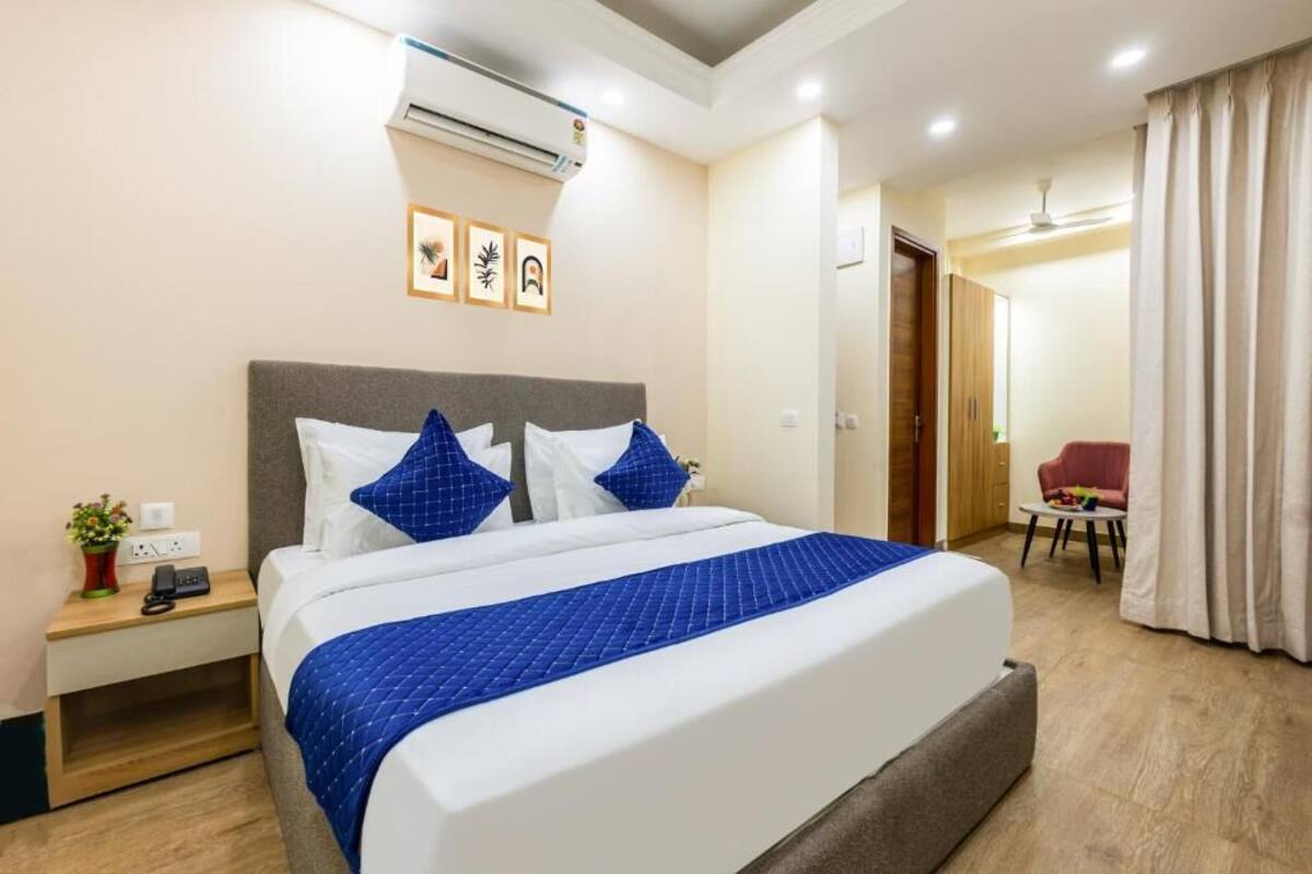 A hotel room with a large bed, a nightstand with a phone and a plant, a ceiling fan, and a door leading to another room.