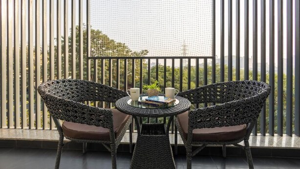 A balcony with two wicker chairs and a small table, a netted window, and a view of greenery.