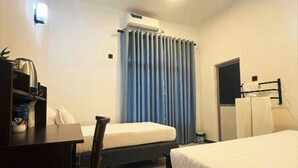 Une chambre d’hôtel équipée d’un bureau, de deux lits, d’un ventilateur de plafond et d’une fenêtre avec des rideaux.