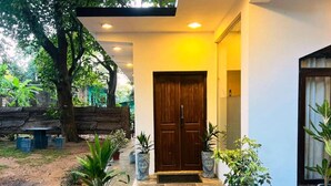Une entrée moderne avec une porte en bois, des plantes en pot et un banc à l’arrière-plan.