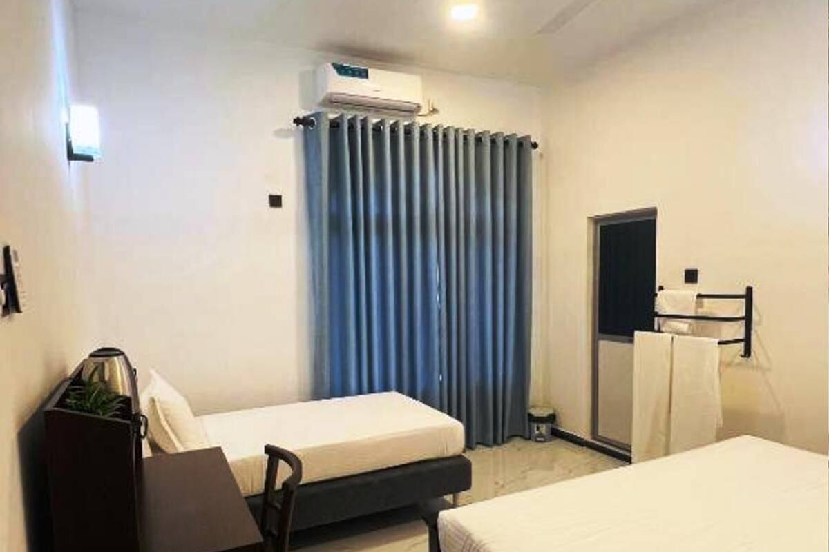 Une chambre d’hôtel avec deux lits, un bureau, une chaise, un ventilateur de plafond et une fenêtre avec des rideaux.
