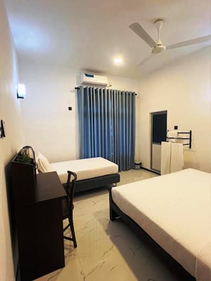 A hotel room with two beds, a desk, a chair, a ceiling fan, and a window with curtains. - Wild Blossom Sigiriya (Sigiriya)