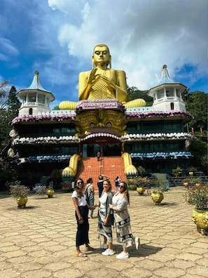 A large golden Buddha statue in front of a temple with traditional architecture. - Wild Blossom Sigiriya (Sigiriya)