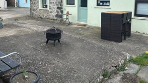 A stone building with a green door, a small patio area with a table and chairs, and a black outdoor heater. - 18th-century former Welsh Mill, only steps to Lower town harbour & Coastal path (Fishguard)