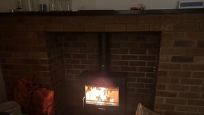 A brick fireplace with a fire burning inside, surrounded by a wooden floor and various items on the mantel.
