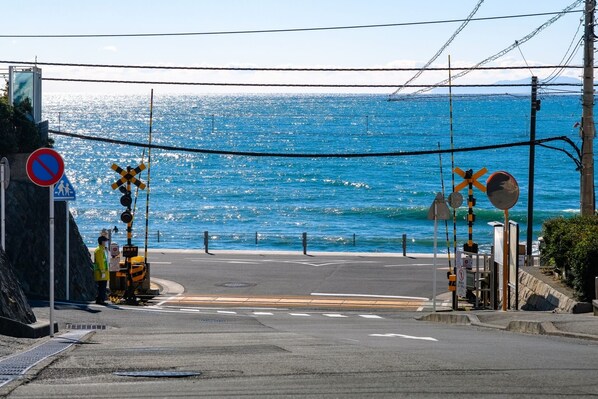 A coastal road with a railway crossing, a pedestrian sign, and a no parking sign.