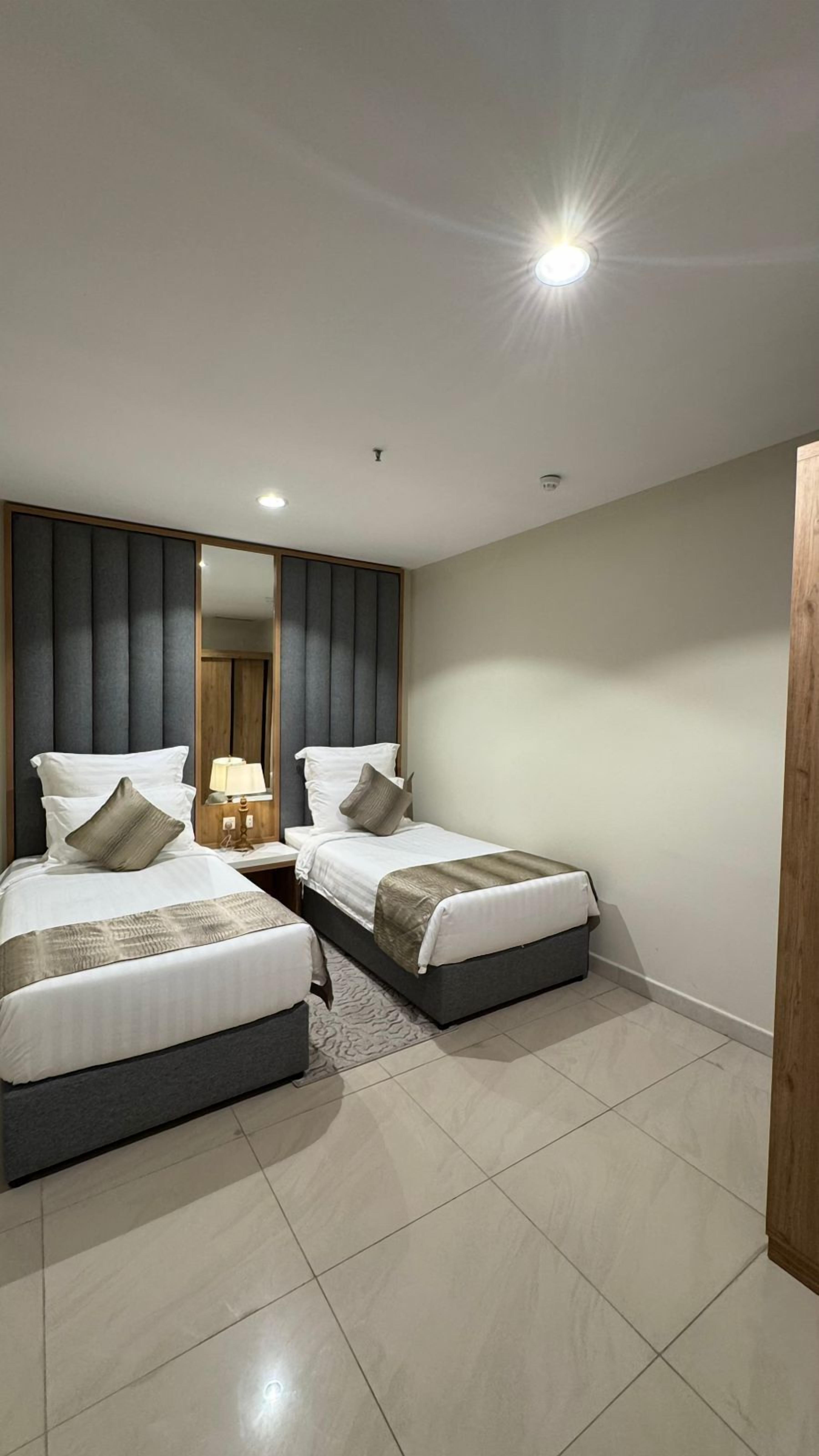 Una habitación de hotel moderna con dos camas, un espejo grande y una mesita de noche pequeña con una lámpara.