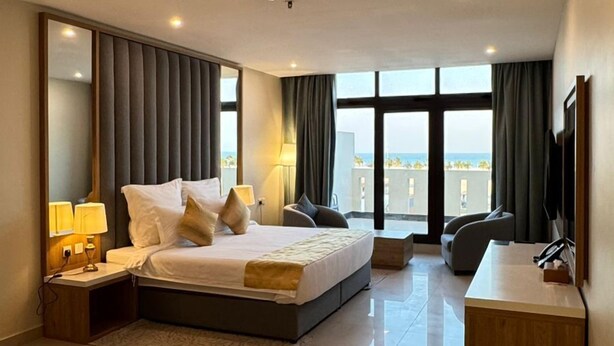 A modern hotel room with a large bed, a desk, and a view of the city. - Continent Hotel Al Uqayr (Al Uqayr)