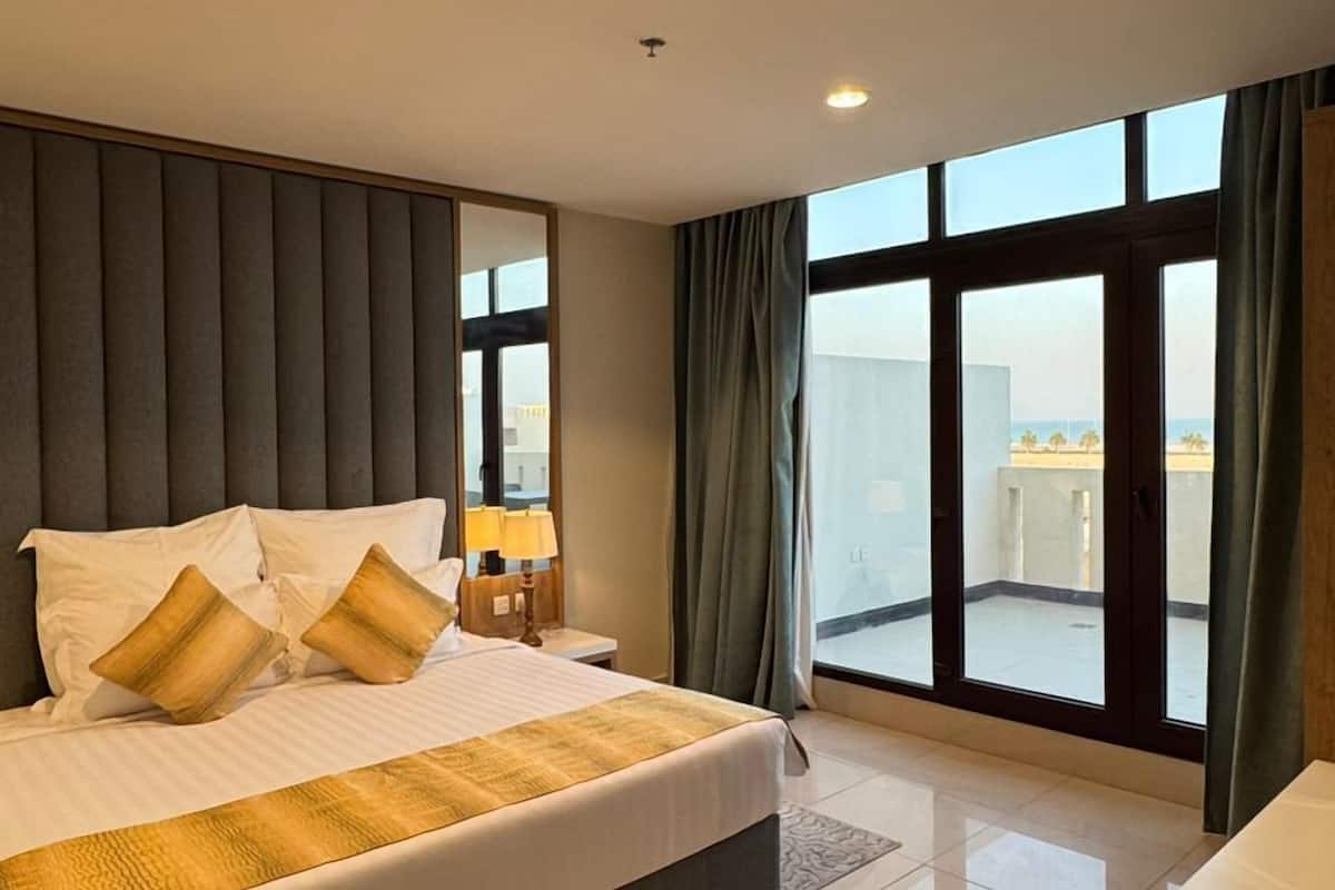 Habitación de hotel moderna con una cama grande, una mesita de noche, tocador y un balcón con vistas.