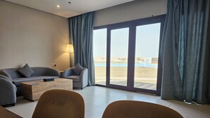 A modern living room with a sofa, armchairs, a coffee table, and a view of a pool and beach. - Continent Hotel Al Uqayr (Al Uqayr)