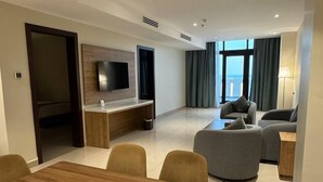 A modern living room with a wooden dining table, sofas, and a TV mounted on the wall. - Continent Hotel Al Uqayr (Al Uqayr)