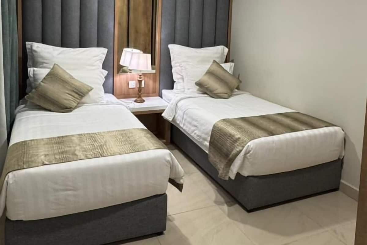 Una habitación de hotel con dos camas, un espejo grande, una mesita de noche y una lámpara en el techo.