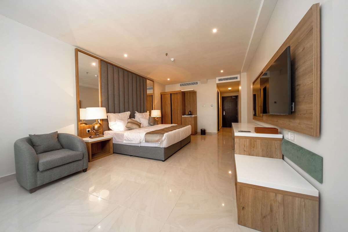Una habitación de hotel moderna con una cama grande, un sofá, un escritorio y un televisor montado en la pared.