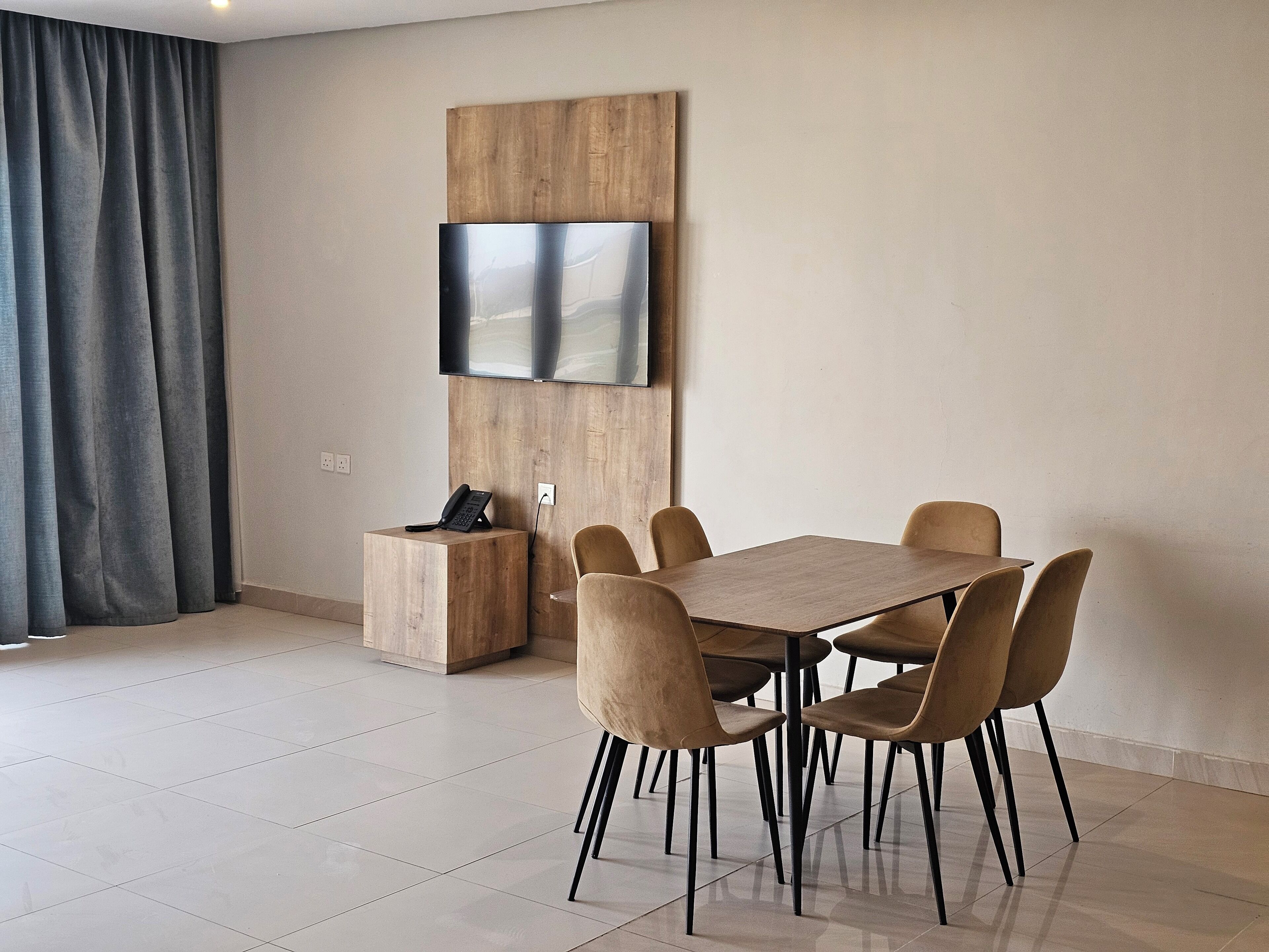 A modern dining area with a wooden table and six chairs, a mounted flat-screen TV, and a telephone on a wooden side table.