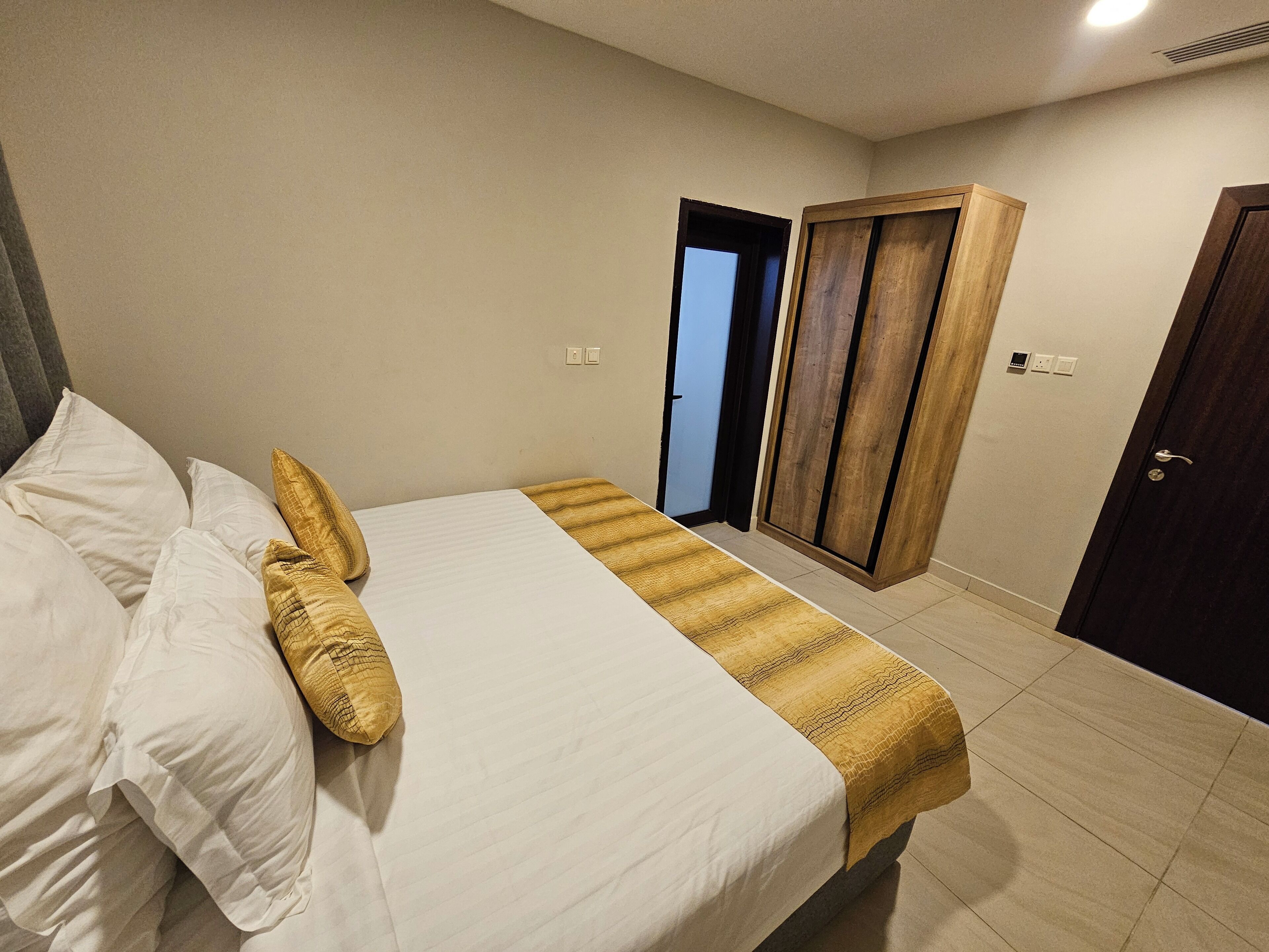 A bedroom with a bed, pillows, a bedside table, a wooden wardrobe, and a door.