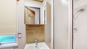 A bathroom with a white sink, wooden panel backsplash, a mirror, and a shower area. - Silver 4 Bedroom Holiday Home (Hornsea)