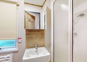 Ein Badezimmer mit einem weißen Waschbecken, einer Holzvertäfelung an der Rückwand, einem Spiegel und einer Duschkabine.