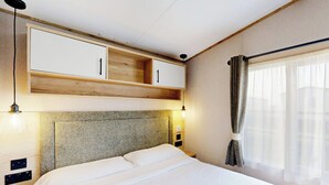 Une chambre d’hôtel comprenant un lit, une tête de lit, une armoire, une table de chevet et une fenêtre avec des rideaux.