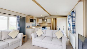 A compact RV interior with a kitchenette, two sofas, and a blue ottoman. - Gold 3 Bedroom Holiday Home (Hornsea)