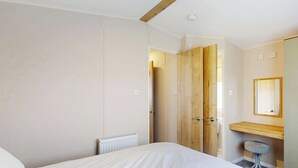 Un dormitorio con cama, una puerta de madera, un radiador, un banco de madera, un taburete y un espejo.