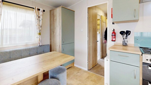 Cocina compacta con mesa y banco de madera, un pequeño rincón de descanso y una kitchenette con estufa y armarios.