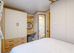 A bedroom with a bed, a wardrobe, a mirror, and a door leading to a bathroom. - Silver 3 Bedroom Holiday Home Pet (Hornsea)