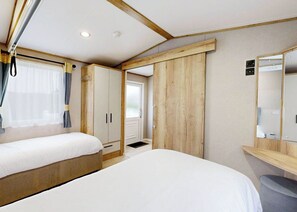 A bedroom with two beds, wooden wardrobes, a mirror, and a window with curtains.
