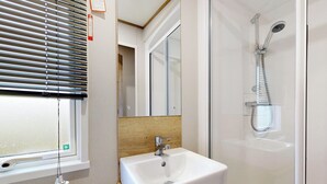 A bathroom with a sink, mirror, shower, and window with blinds. - Gold 3 Bedroom Holiday Home Pet (Hornsea)