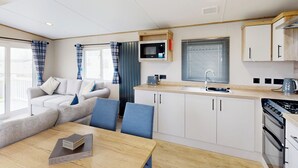 A modern kitchen with a microwave, stove, and sink. There is a dining area with a table and chairs. - Gold 3 Bedroom Holiday Home Pet (Hornsea)