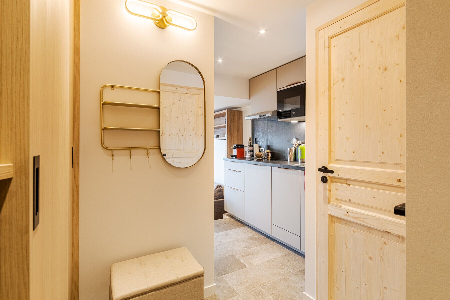 Un couloir étroit avec un banc, un miroir fixé au mur et une porte donnant sur un espace cuisine.