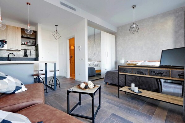 A modern living room with a sofa, a coffee table, a TV, and a kitchen area with cabinets and a countertop. - Delizioso monolocale con ampio terrazzo a Testaccio (ROMA)