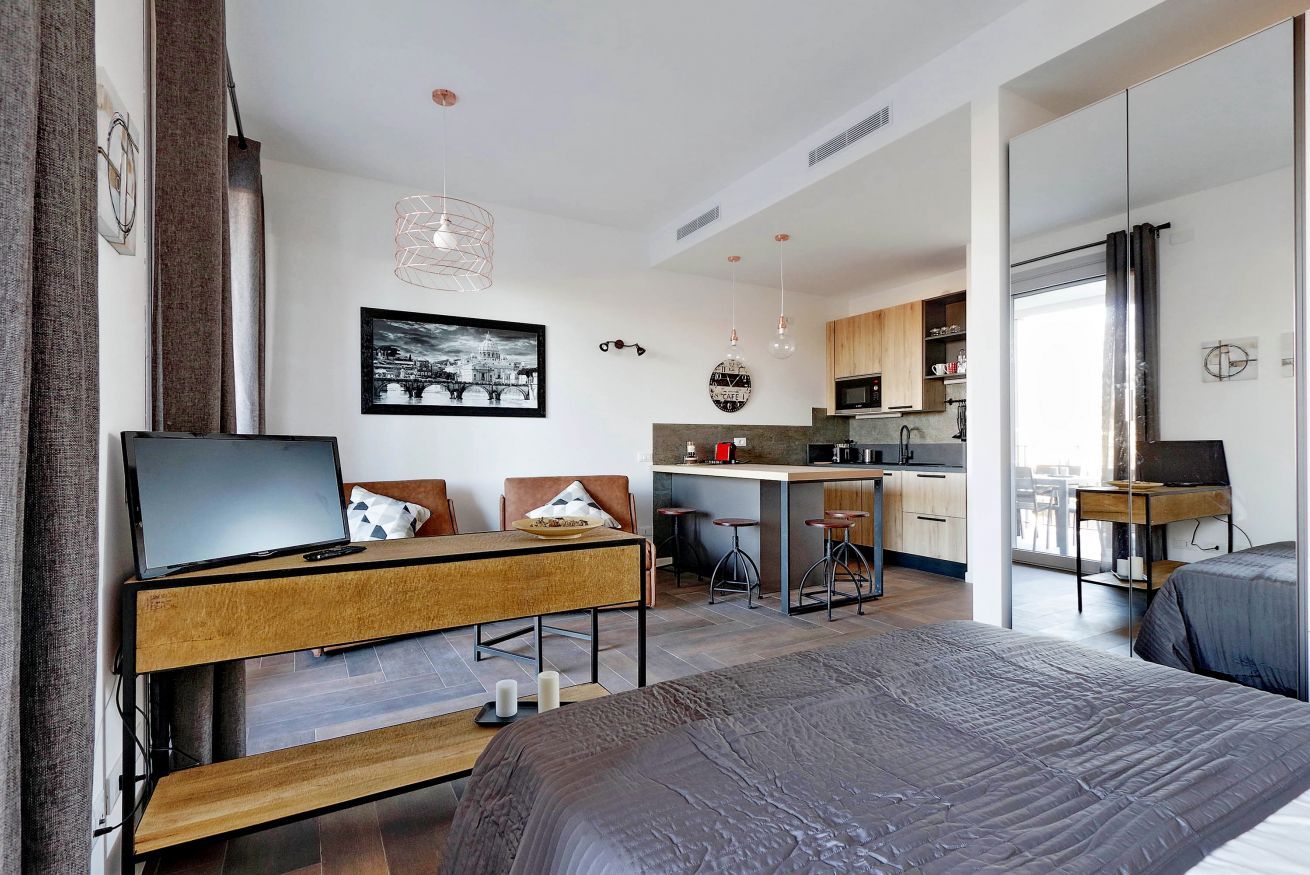 Ein modernes, kompaktes Hotelzimmer mit Bett, Schreibtisch mit Laptop, Küchenzeile und Essbereich.