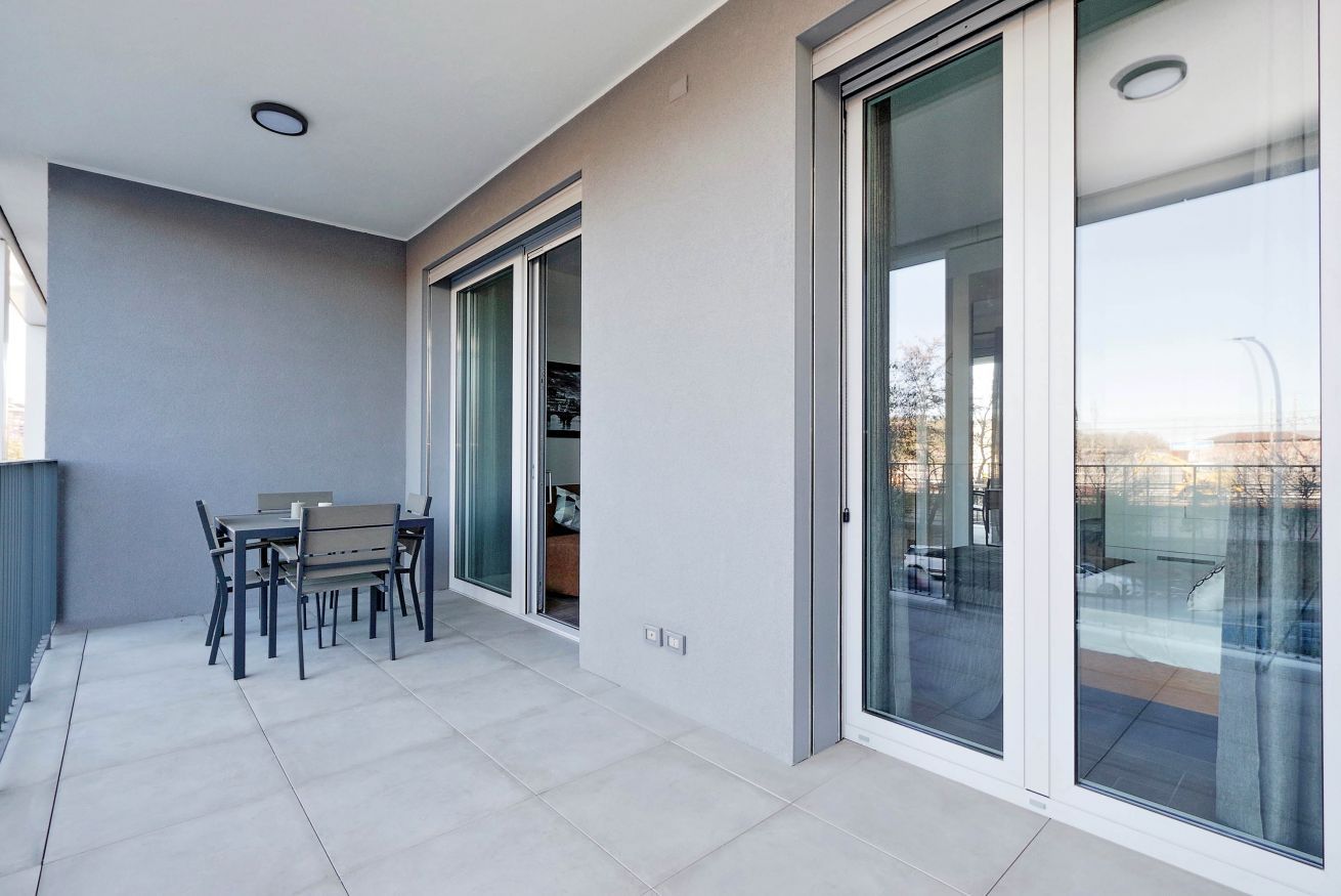 Un balcon moderne doté d’une table et de chaises, de portes-fenêtres coulissantes et d’un sol carrelé.