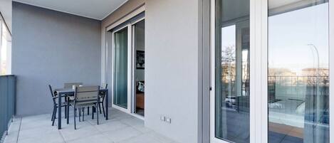 Un balcon moderne doté d’une table et de chaises, de portes-fenêtres coulissantes et d’un sol carrelé.