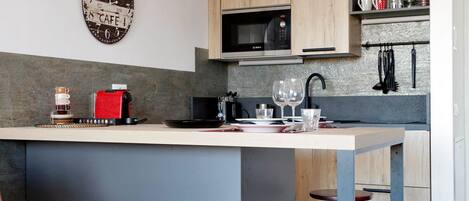 Cozinha moderna com ilha central, armários de madeira, micro-ondas Bosch e banquetas de bar.