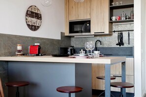 A modern kitchen with a central island, wooden cabinets, a Bosch microwave, and bar stools. - Delizioso monolocale con ampio terrazzo a Testaccio (ROMA)