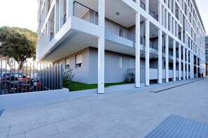 A modern multi-story building with balconies, a paved ground floor, and a parking area with cars. - Delizioso monolocale con ampio terrazzo a Testaccio (ROMA)