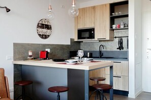 Une cuisine moderne dotée d’un îlot central, de tabourets de bar, d’un four à micro-ondes et de luminaires suspendus.