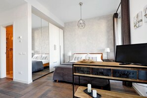 Ein modernes Hotelzimmer mit Bett, Nachttisch, Fernseher und einem großen Spiegel.