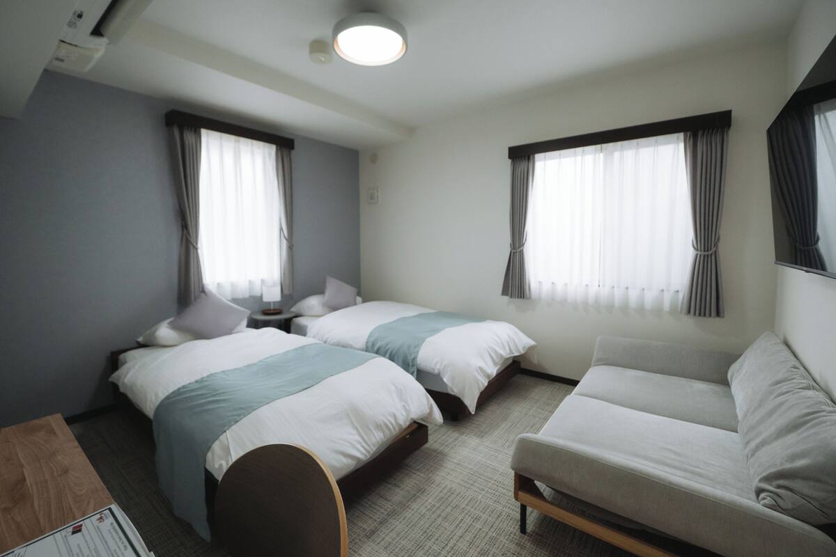 A hotel room with two beds, a sofa, a desk, and a window with curtains.