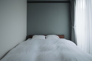 Ein Bett mit weißer Bettwäsche, einem Holzkopfteil und einer grauen Wand.