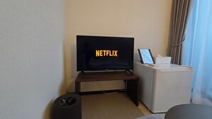 Une chambre d’hôtel moderne équipée d’un téléviseur à écran plat affichant le logo de Netflix, d’un ordinateur portable posé sur une petite table, d’une poubelle et d’un canapé gris.