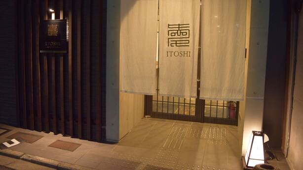 L’entrée d’un hôtel, avec une enseigne portant le nom « ITOSHI » et une porte d’entrée de style japonais traditionnel.